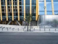 a person riding a bike down a street past a building with tall windows and silver fencing