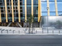 a person riding a bike down a street past a building with tall windows and silver fencing