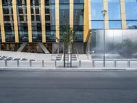 a person riding a bike down a street past a building with tall windows and silver fencing