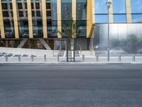 a person riding a bike down a street past a building with tall windows and silver fencing