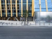 a person riding a bike down a street past a building with tall windows and silver fencing