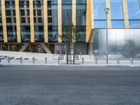 a person riding a bike down a street past a building with tall windows and silver fencing