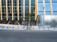 a person riding a bike down a street past a building with tall windows and silver fencing