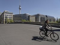 the person is on a bicycle in front of a building with a television tower in the background