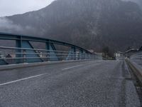 a person on a bike crosses a bridge in mountainside town in the background,