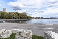 a person on a bicycle rides past a river in the city park near a fenced area