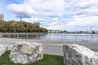 a person on a bicycle rides past a river in the city park near a fenced area