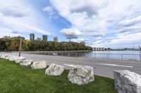 a person on a bicycle rides past a river in the city park near a fenced area