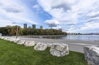 a person on a bicycle rides past a river in the city park near a fenced area