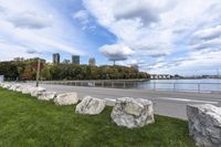 a person on a bicycle rides past a river in the city park near a fenced area