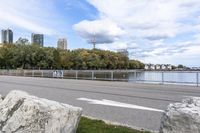 a person on a bicycle rides past a river in the city park near a fenced area