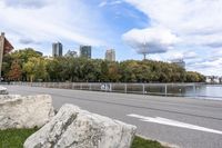 a person on a bicycle rides past a river in the city park near a fenced area