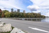 a person on a bicycle rides past a river in the city park near a fenced area