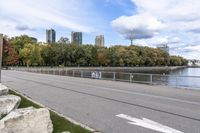 a person on a bicycle rides past a river in the city park near a fenced area