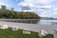 a person on a bicycle rides past a river in the city park near a fenced area