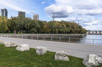 a person on a bicycle rides past a river in the city park near a fenced area