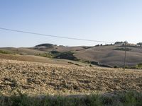 a dirt path in the middle of an open field near trees and hills and a person on a bicycle