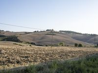 a dirt path in the middle of an open field near trees and hills and a person on a bicycle