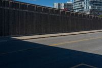 a man is riding his bike on the side of a road beside tall buildings and a fence