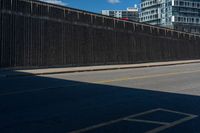 a man is riding his bike on the side of a road beside tall buildings and a fence