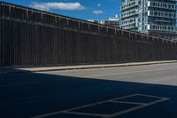 a man is riding his bike on the side of a road beside tall buildings and a fence