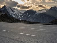 the person is riding their bike on the road in the mountains under cloudy skies and snow covered hills