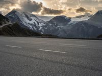 the person is riding their bike on the road in the mountains under cloudy skies and snow covered hills