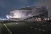 a modern building in front of a city street at night time with a car passing through the foreground