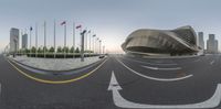 a view from outside of a very large building on the street corner, looking at a road with a building on top, a long curving curve and flags on it