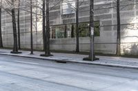 the empty sidewalk is next to tall buildings and a man walking down the street on his skate board