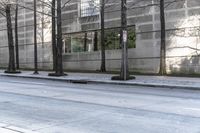 the empty sidewalk is next to tall buildings and a man walking down the street on his skate board