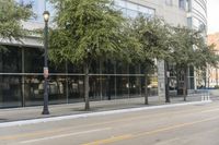 a man standing on the sidewalk of a street corner next to some trees and buildings