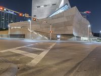 an intersection that is very lit up at night time, with cars moving in and out of the building