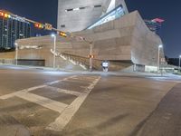 an intersection that is very lit up at night time, with cars moving in and out of the building