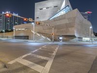 an intersection that is very lit up at night time, with cars moving in and out of the building