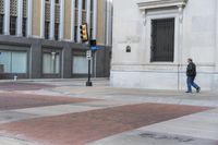 a man walking across a sidewalk in a red shirt and brown jacket towards a building