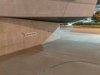 a skateboard sits in an open space near a wall in a parking lot and near a sidewalk in the evening