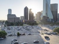 a view of several cars in a parking lot at sunset with buildings behind it on a clear day