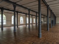 there are wooden floor in an empty warehouse space with windows above them, and several arches and columns