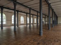 there are wooden floor in an empty warehouse space with windows above them, and several arches and columns