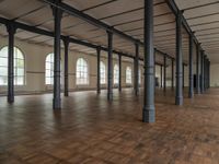 there are wooden floor in an empty warehouse space with windows above them, and several arches and columns