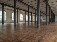 there are wooden floor in an empty warehouse space with windows above them, and several arches and columns