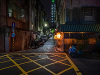 a dark city street with many scooters parked at a fenced off area