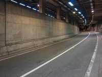 the view down an empty highway, looking straight ahead at night lights, in a dark, concrete city tunnel