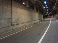 the view down an empty highway, looking straight ahead at night lights, in a dark, concrete city tunnel