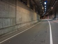 the view down an empty highway, looking straight ahead at night lights, in a dark, concrete city tunnel