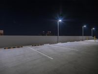 an empty parking lot at night with street lights shining on the wall and a row of poles