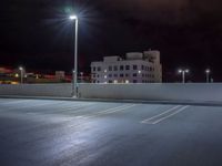 a parking lot is illuminated with street lamps by a tall white building in the city