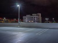 a parking lot is illuminated with street lamps by a tall white building in the city