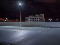 a parking lot is illuminated with street lamps by a tall white building in the city